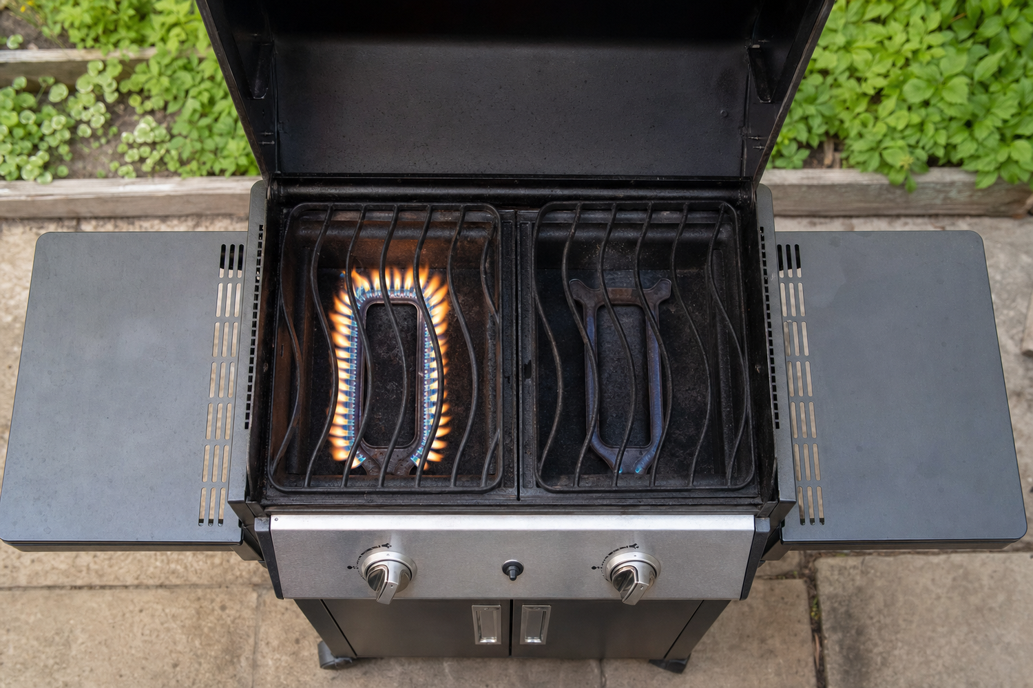 Gas grill interior with lid open showing uneven burner flames on one side versus dim flame on other side